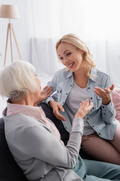 Smiling woman looking at senior mother pointing with hands on couch — Stock Photo