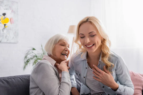 Mujer alegre sentada cerca de la madre anciana en el sofá - foto de stock