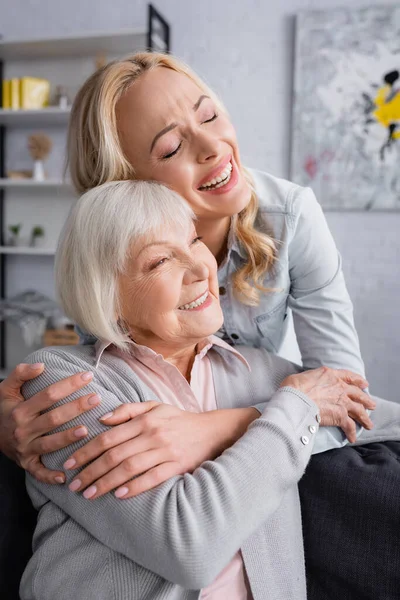 Lachende Frau umarmt Seniorin im Wohnzimmer — Stockfoto