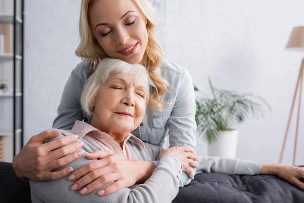 Erwachsene Frau lächelt und umarmt grauhaarige Mutter — Stockfoto