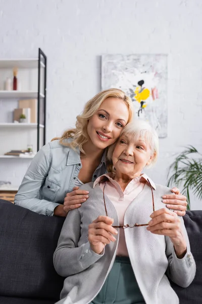Mujer mayor sosteniendo anteojos cerca de su hija sonriente - foto de stock