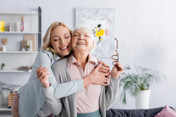 Happy grey haired woman holding eyeglasses near daughter — Stock Photo