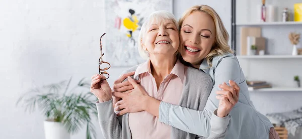 Donna allegra che abbraccia la madre anziana con gli occhiali, striscione — Foto stock