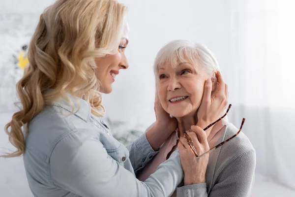 Улыбающаяся женщина трогает лицо старшей матери в очках — стоковое фото