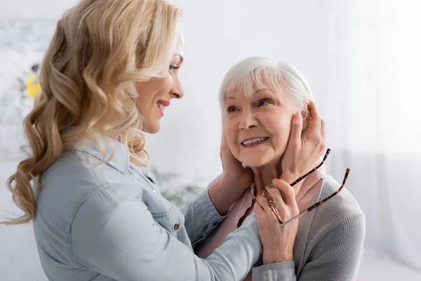 Smiling woman touching face of senior mother with eyeglasses — Stock Photo