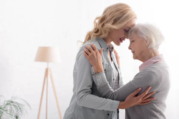 Seitenansicht einer lächelnden erwachsenen Frau, die ihre Mutter umarmt — Stockfoto