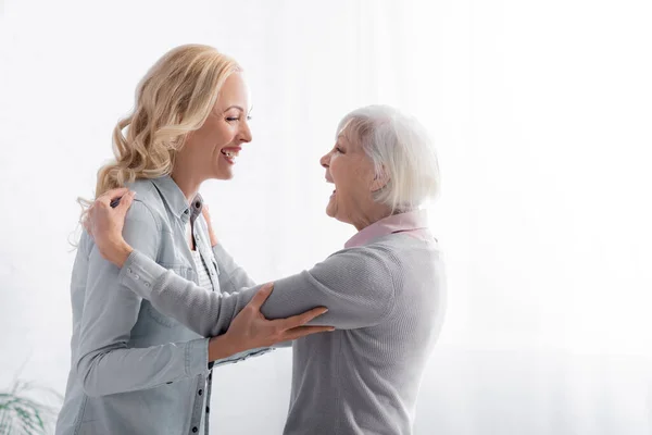 Vista lateral de la mujer alegre y la madre mirándose mientras se abrazan - foto de stock