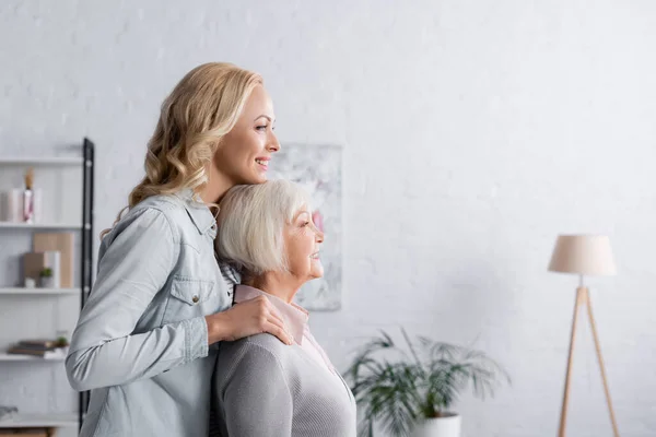 Vista laterale della donna allegra in piedi vicino ai genitori anziani in soggiorno — Foto stock