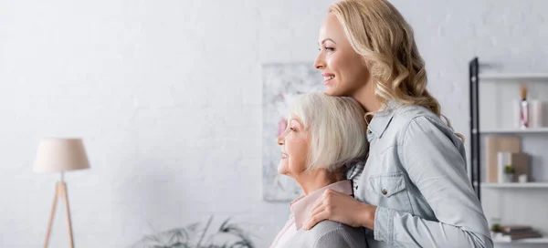 Vista laterale della donna che abbraccia la madre in soggiorno, banner — Foto stock