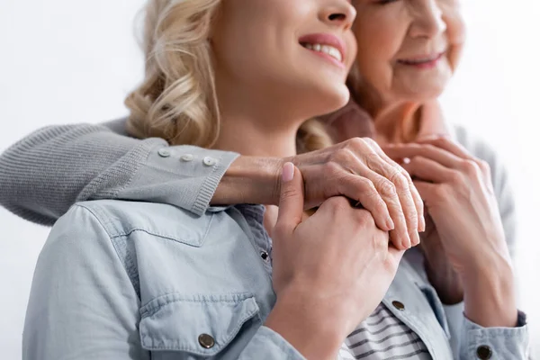 Cropped view of senior woman holding hand of smiling daughter on blurred background — Stock Photo