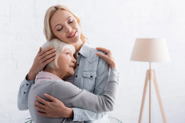 Donna e figlia ad occhi chiusi che si abbracciano in salotto — Foto stock