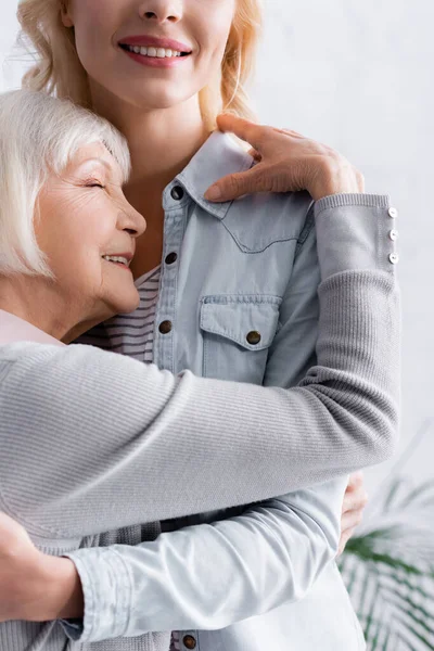 Glückliche grauhaarige Frau umarmt lächelnde Tochter — Stockfoto