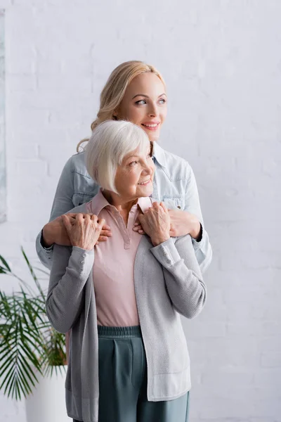 Souriant parent aîné et fille regardant loin dans le salon — Photo de stock