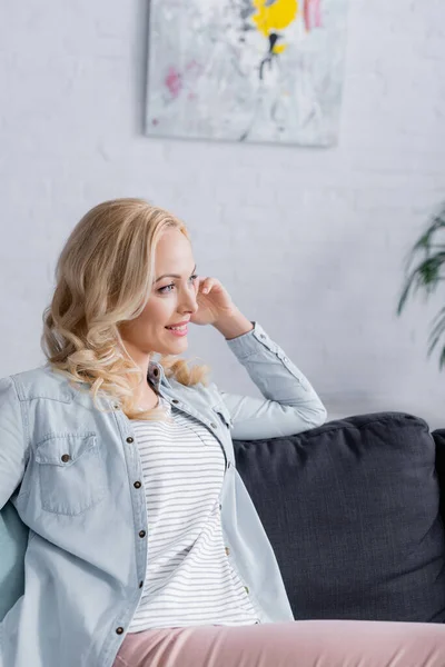 Mujer rubia sonriendo mientras se sienta en la sala de estar - foto de stock