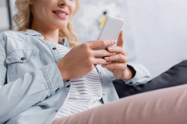 Ausgeschnittene Ansicht des Smartphones in den Händen einer lächelnden Frau auf verschwommenem Hintergrund — Stockfoto