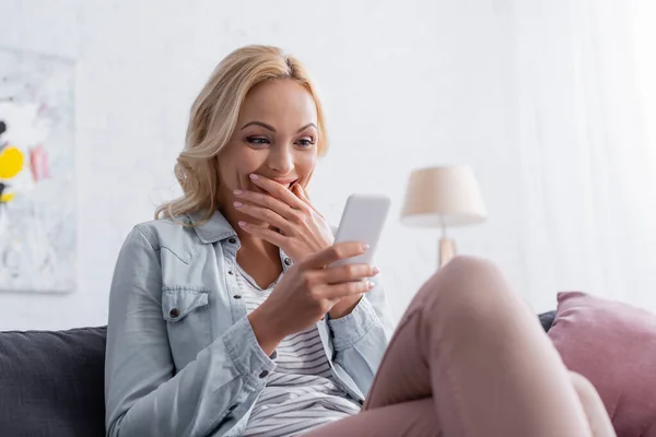 Donna stupita utilizzando il cellulare sul divano — Foto stock