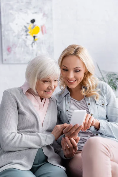 Mujer sonriente sosteniendo teléfono inteligente cerca de la madre mayor - foto de stock