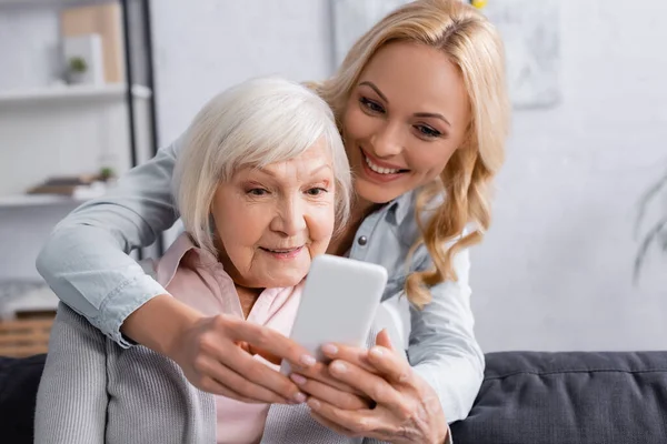 Smartphone on blurred foreground in hands of woman near mother — Stock Photo