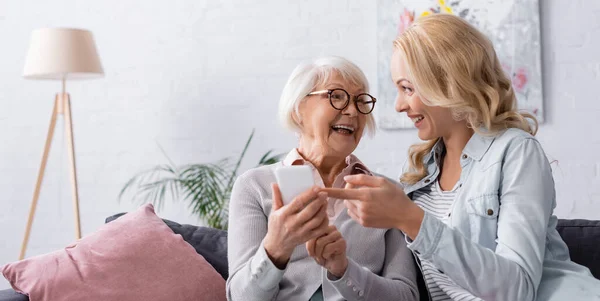 Fröhliche Frau zeigt auf Smartphone in den Händen der Mutter — Stockfoto