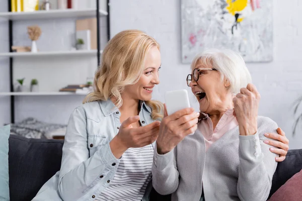 Excitada mulher idosa segurando smartphone perto da filha — Fotografia de Stock