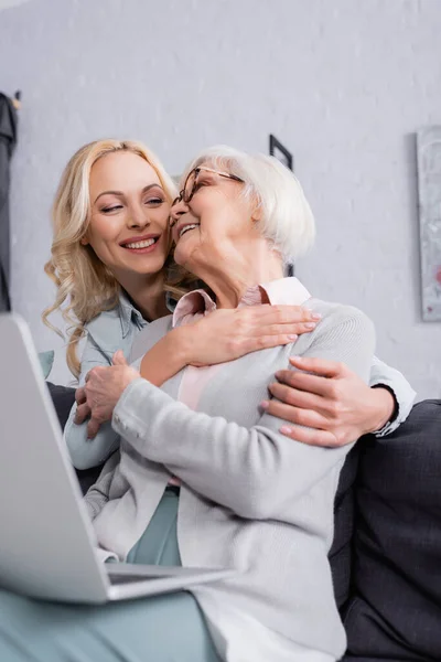 Des femmes souriantes embrassant près d'un ordinateur portable au premier plan flou — Photo de stock