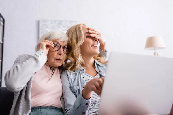 Femme excitée couvrant les yeux de sa fille près d'un ordinateur portable flou à la maison — Photo de stock