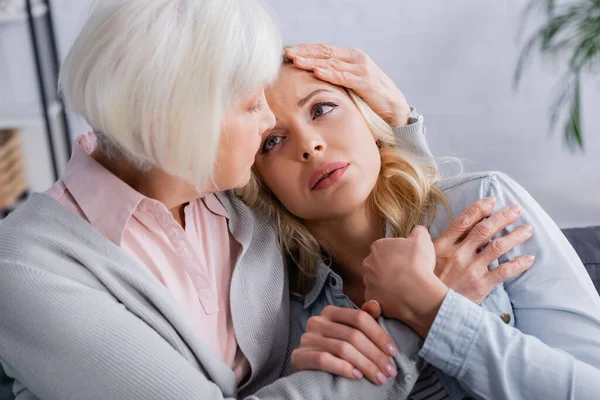 Woman holding hand of senior mother on blurred foreground at home — Stock Photo