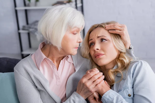 Elderly mother hugging displeased daughter at home — Stock Photo