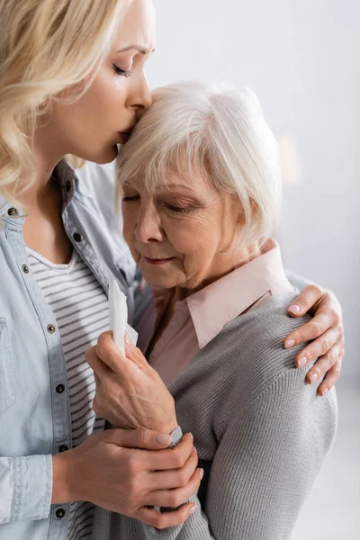 Daughter kissing displeased senior woman holding napkin — Stock Photo