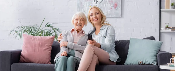 Cheerful woman hugging mother and holding remote controller, banner — Stock Photo