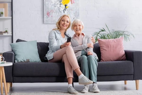 Smiling woman sitting near daughter with remote controller — Stock Photo