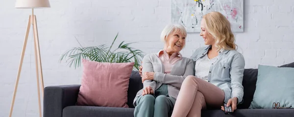 Donna anziana sorridente alla figlia con telecomando sul divano, banner — Foto stock