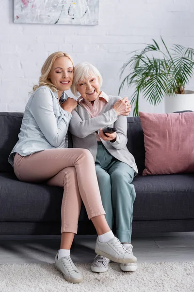 Donna adulta che abbraccia genitore sorridente con telecomando — Foto stock