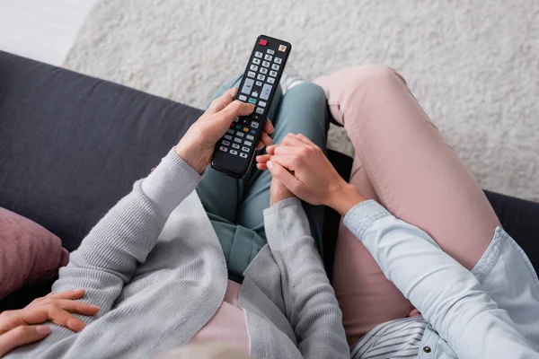 Vue du dessus de la femme tenant la main de la mère aînée avec télécommande sur le canapé — Photo de stock