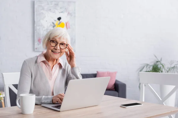 Mulher sorrindo olhando para a câmera perto de gadgets e copo — Fotografia de Stock