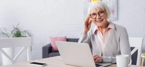 Elderly woman smiling near gadgets and cup, banner — Stock Photo