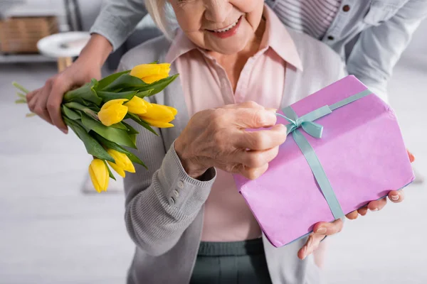 Обрізаний вид жінки, що тримає квіти біля літньої матері з подарунком — стокове фото