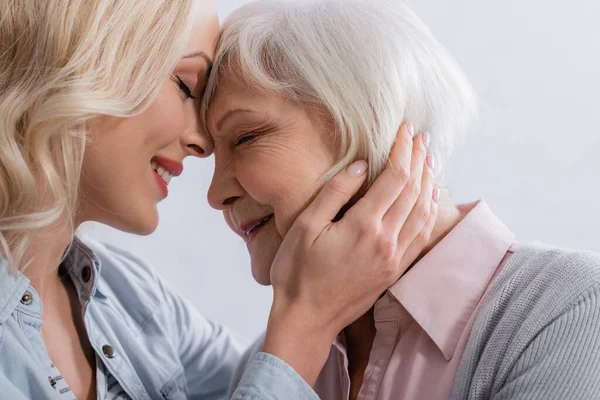 Mujer positiva con los ojos cerrados abrazando a la madre anciana — Stock Photo