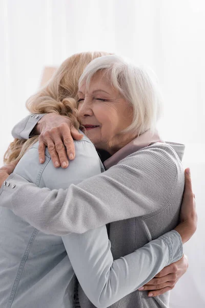 Frau umarmt grauhaarige Mutter zu Hause — Stockfoto