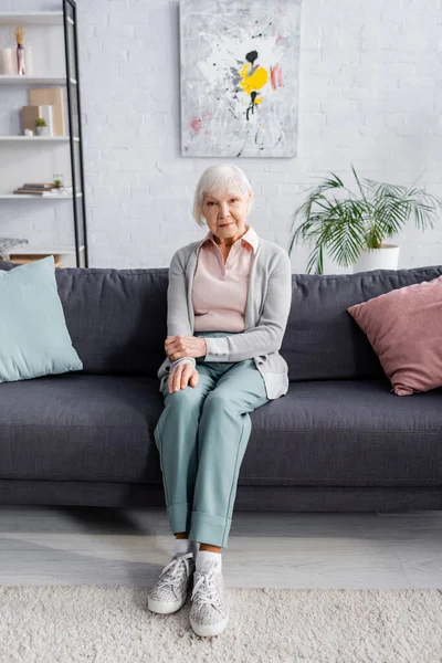 Femme âgée regardant la caméra sur le canapé — Photo de stock