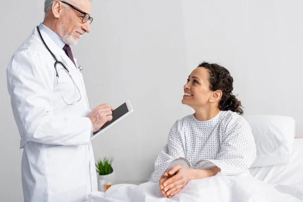 Smiling doctor holding digital tablet near happy african american woman in hospital — Stock Photo