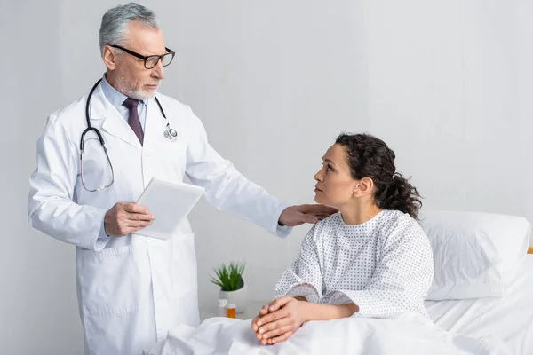 Mature doctor touching shoulder of african american woman while holding digital tablet — Stock Photo