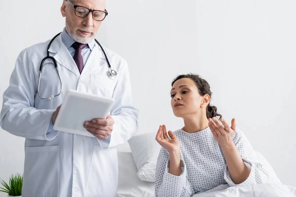 Worried african american woman looking at digital tablet in hands of mature doctor — Stock Photo