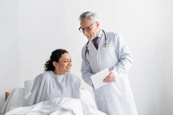 Sonriente médico mostrando tableta digital a la mujer afroamericana complacida en la clínica - foto de stock