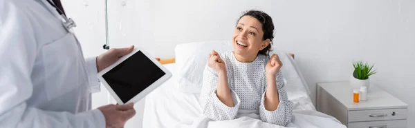 Joyeuse femme afro-américaine montrant geste de succès près du médecin avec tablette numérique au premier plan flou, bannière — Photo de stock