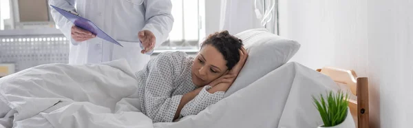 Triste mulher afro-americana deitada na cama do hospital perto do médico, banner — Fotografia de Stock