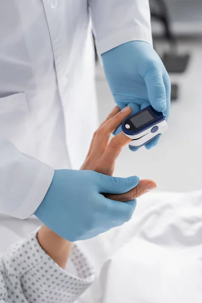 Vista ritagliata del medico in guanti di lattice misurazione della frequenza cardiaca della donna con pulsossimetro — Foto stock