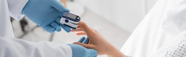 Partial view of doctor in latex gloves measuring saturation of woman with pulse oximeter, banner — Stock Photo