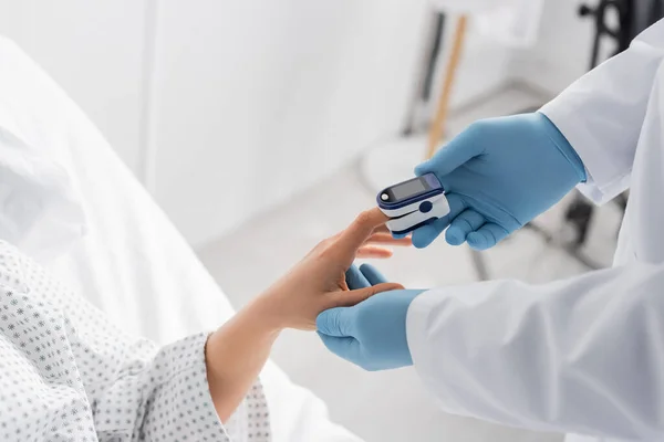 Vista ritagliata del medico in guanti di lattice utilizzando pulsossimetro sul dito del paziente — Foto stock