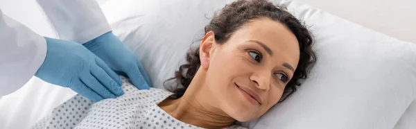 Doctor en guantes de látex examinando hombro de mujer afroamericana sonriente, bandera - foto de stock